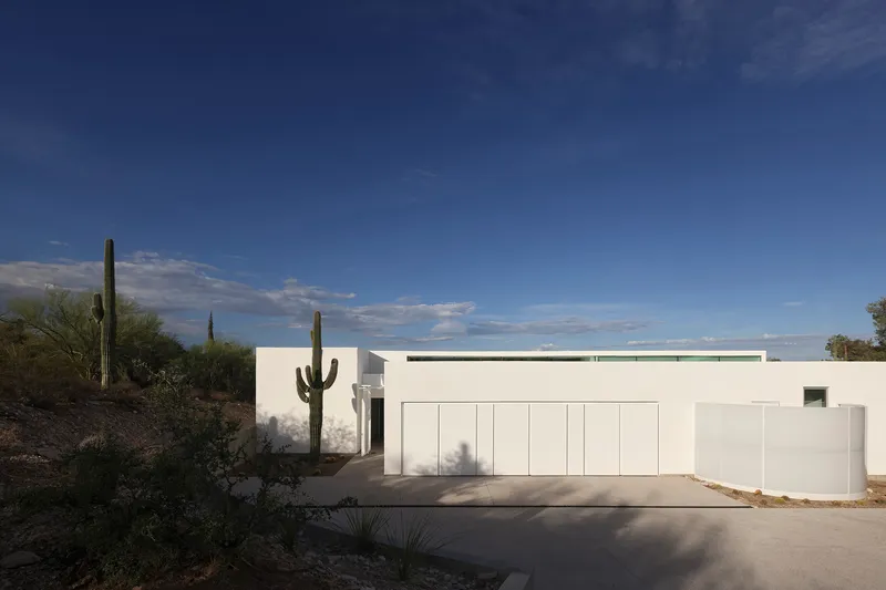 Street view of white stucco facade with paneled garage doors and native saguaro cacti