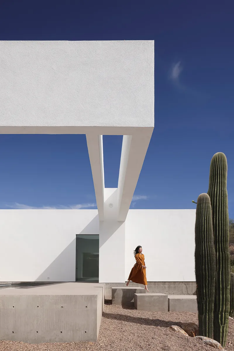 Inverted V-shaped column supporting an upper volume with a person walking past saguaro cacti