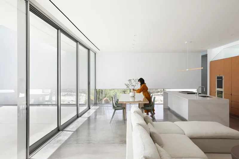 Open-plan living space with floor-to-ceiling glass and a person at the dining table