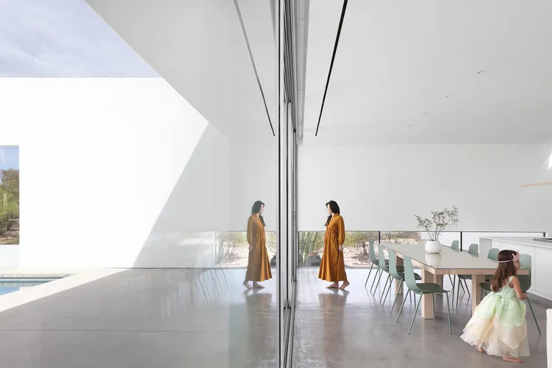 Open plan living and dining space with floor-to-ceiling sliding glass doors and two figures in ochre