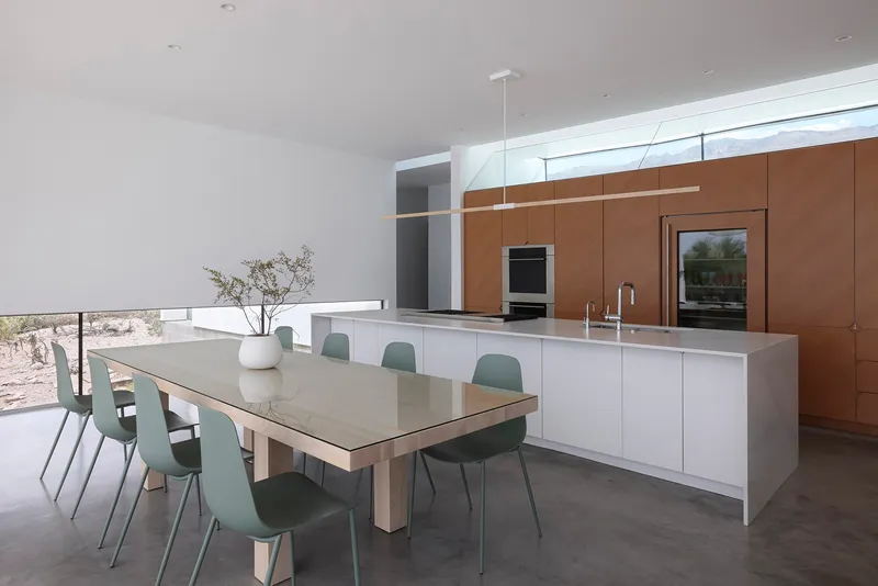Kitchen and dining area with white island, sage chairs, and walnut-toned cabinetry wall