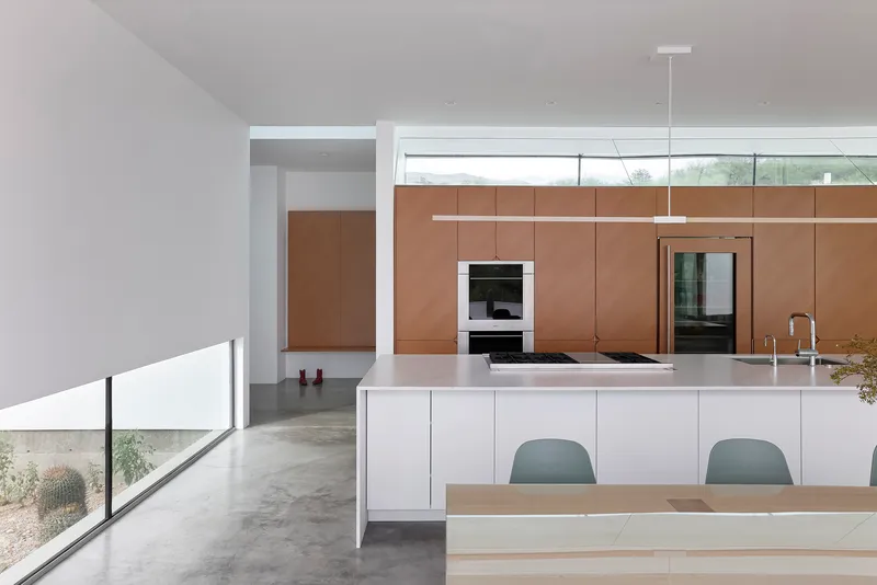 Kitchen island with polished white countertop and linear pendant light above clerestory windows