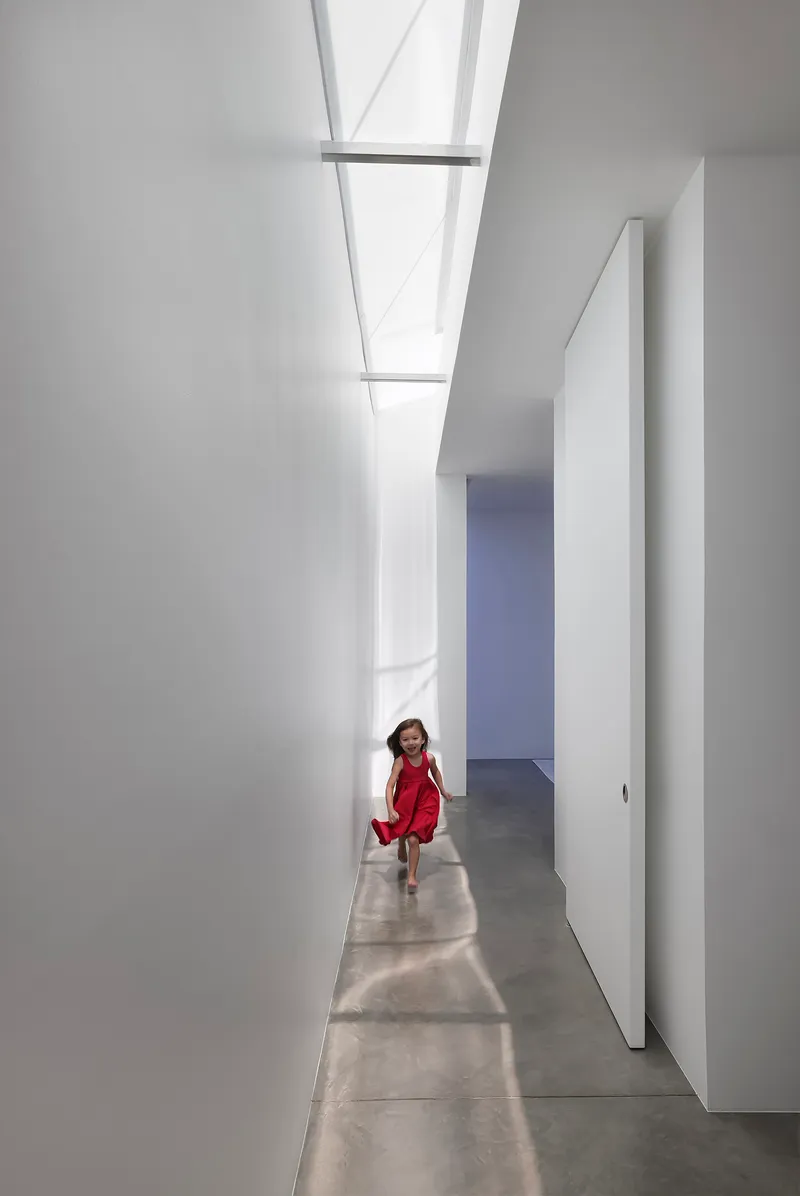 White corridor with rectangular skylights and a child walking through sunlight patches