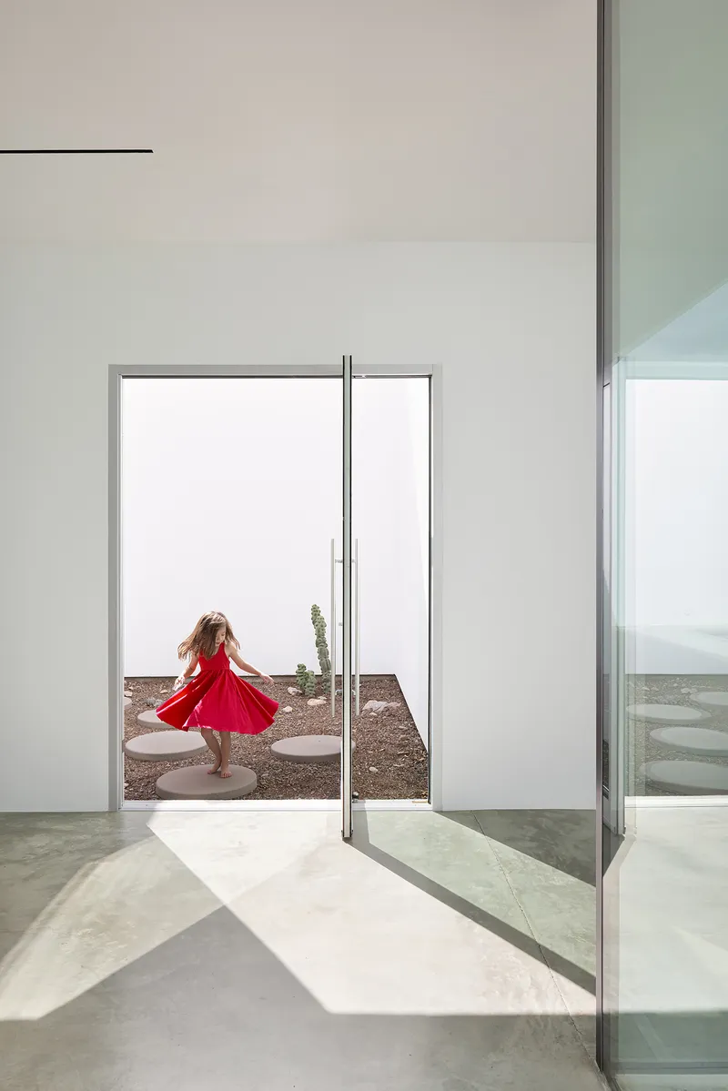 Glazed doorway framing a child in a courtyard with desert plants and gravel