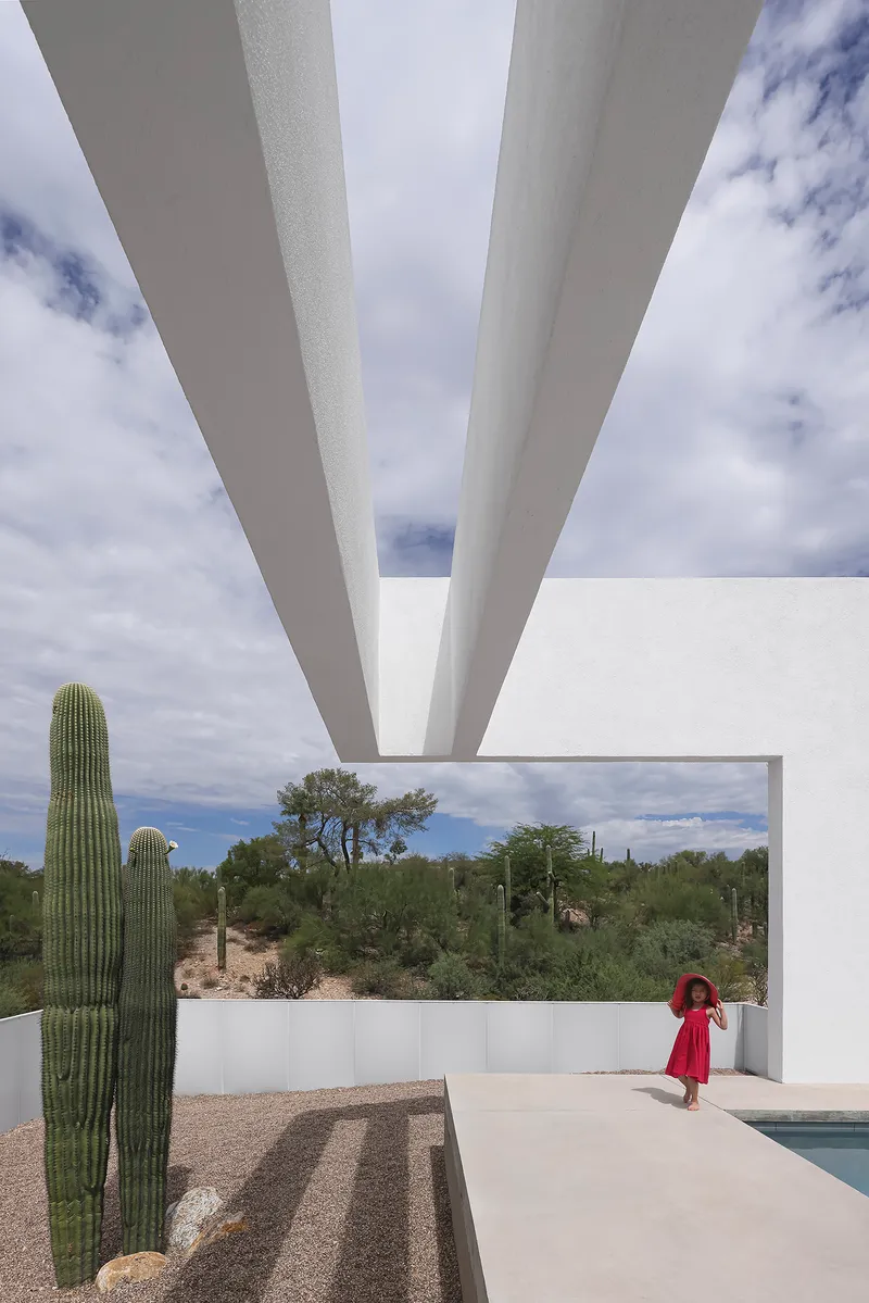View beneath tapered white concrete roof beams overlooking the pool terrace and desert beyond