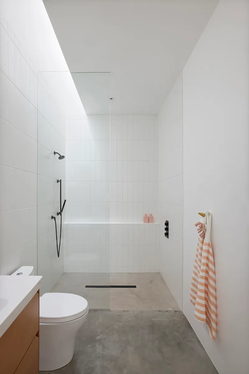 White tiled wet room with skylight, black shower fixtures, and polished concrete floor
