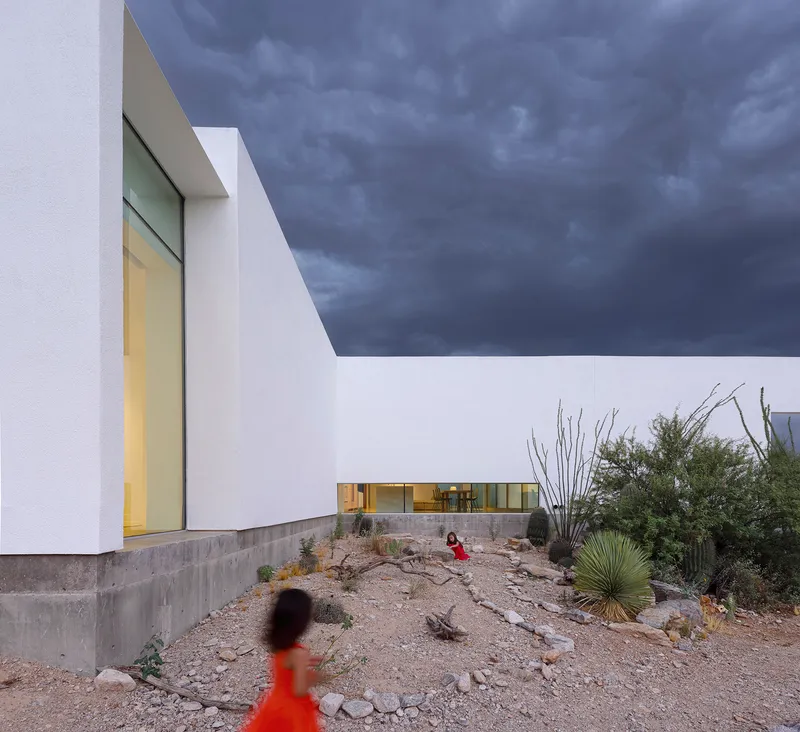 Courtyard with native desert plantings, ocotillo, and children walking beneath dramatic storm sky