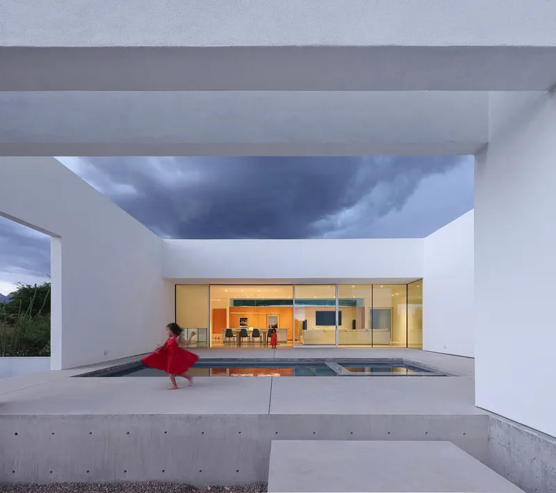 Covered terrace with reflecting pool framing full-height glazed living space at dusk