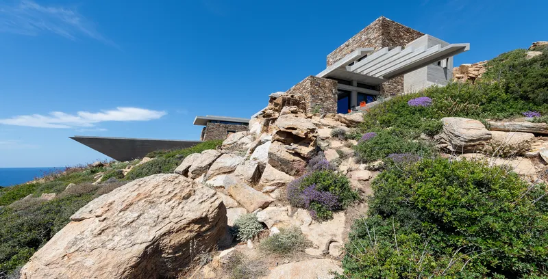 Stone-clad volumes terraced into the hillside with native vegetation and boulders under a clear sky