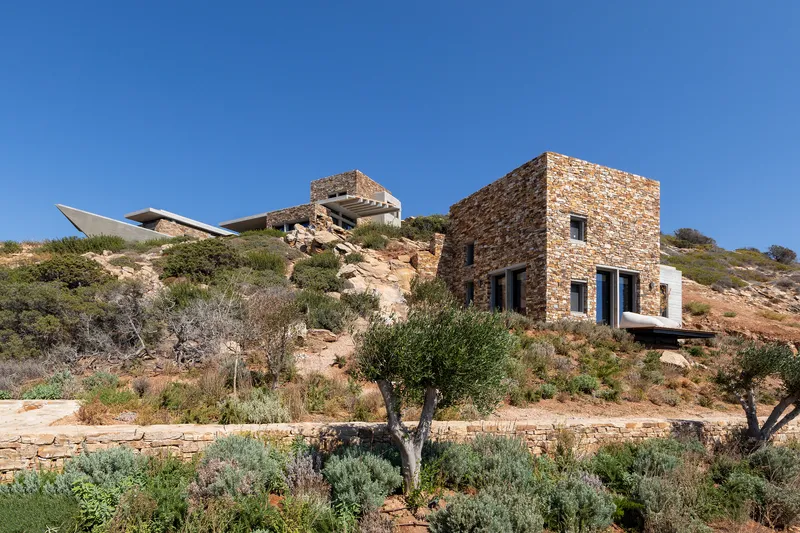 Stone tower and white volumes scattered across the hillside amid olive trees and scrub grasses