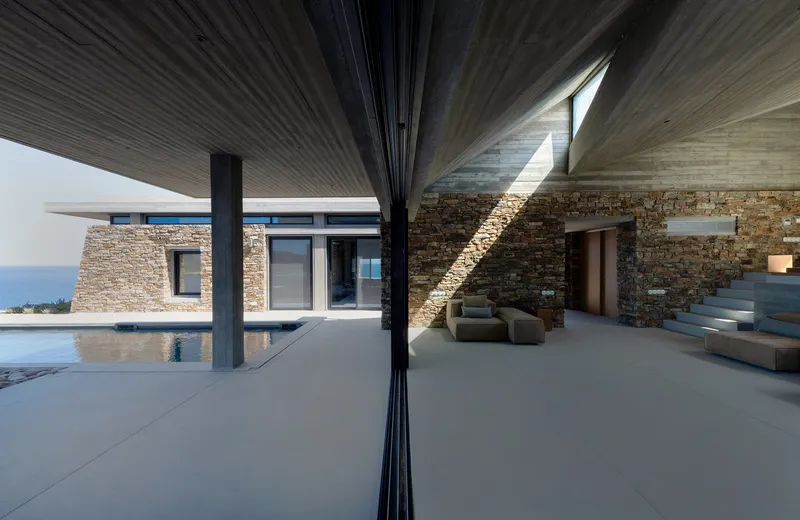 Covered terrace with ribbed timber ceiling, stone walls, and pool edge reflecting the open sky