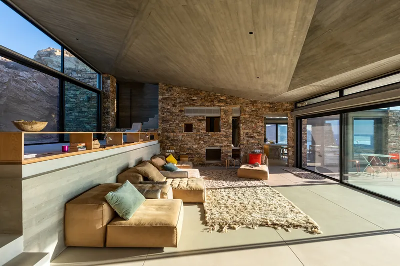 Living space with stone fireplace wall, timber ceiling, and sunken seating area opening to the terrace
