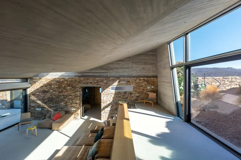 Angled concrete ceiling plane intersecting stone wall with sunlight streaming through clerestory glazing
