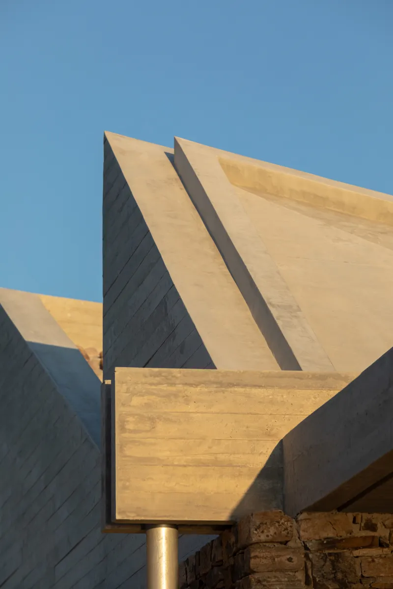 Angled board-formed concrete roof planes intersecting under a clear blue sky