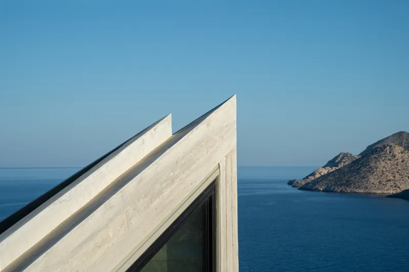 Angular concrete roof planes with a glazed corner overlooking the blue sea and distant rocky island