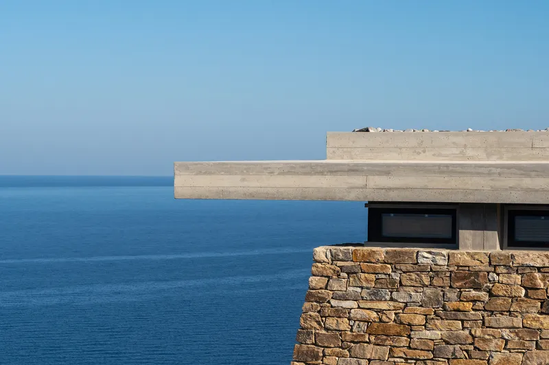 Cantilevering concrete roof over stone retaining wall and ribbon windows facing the open sea