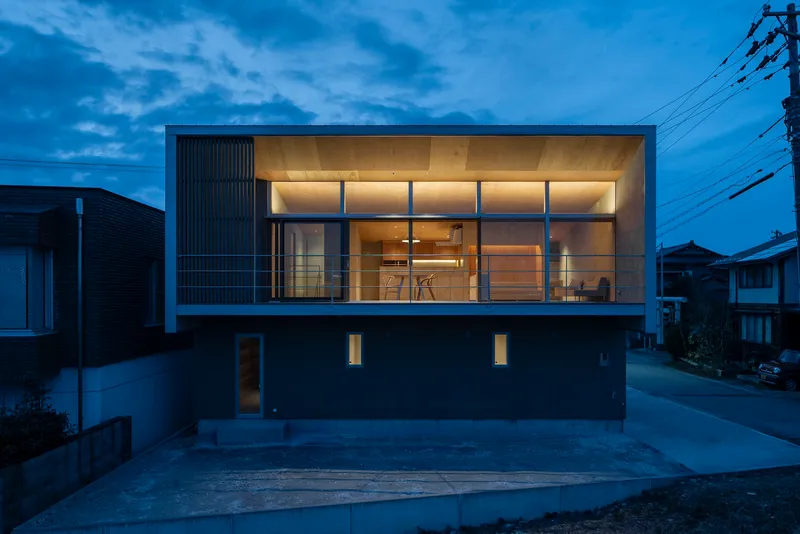 Street facade with ribbed metal cladding and glazed upper volume illuminated at dusk