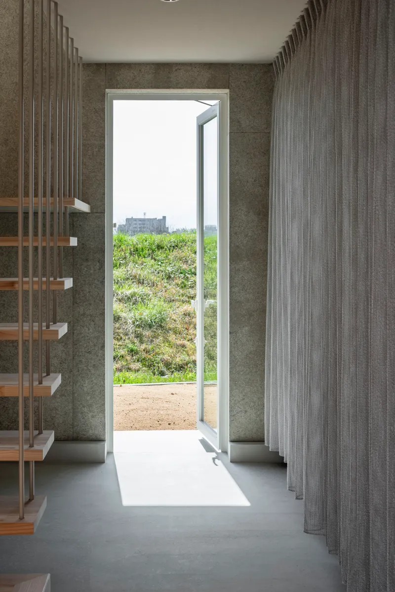 Open doorway in concrete wall with vertical screen panels flooding light across polished floor