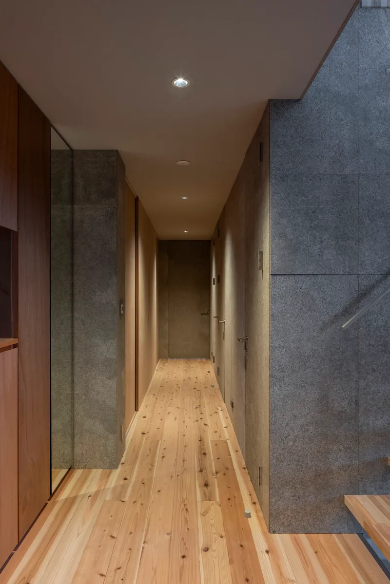 Narrow hallway with concrete walls, timber flooring, and recessed lighting along plywood ceiling