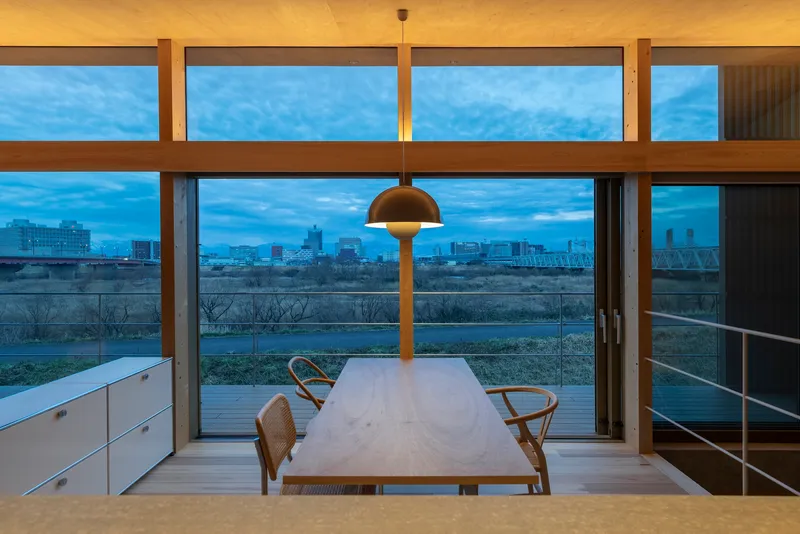 Dining table framed by horizontal timber windows with a view of the river at twilight