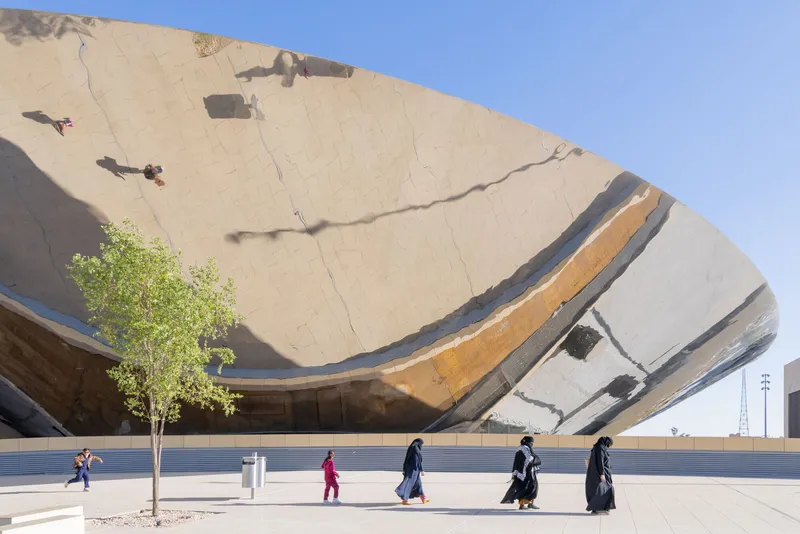Tilted concrete canopy with layered stripes casting shadows on pedestrians walking along the plaza below