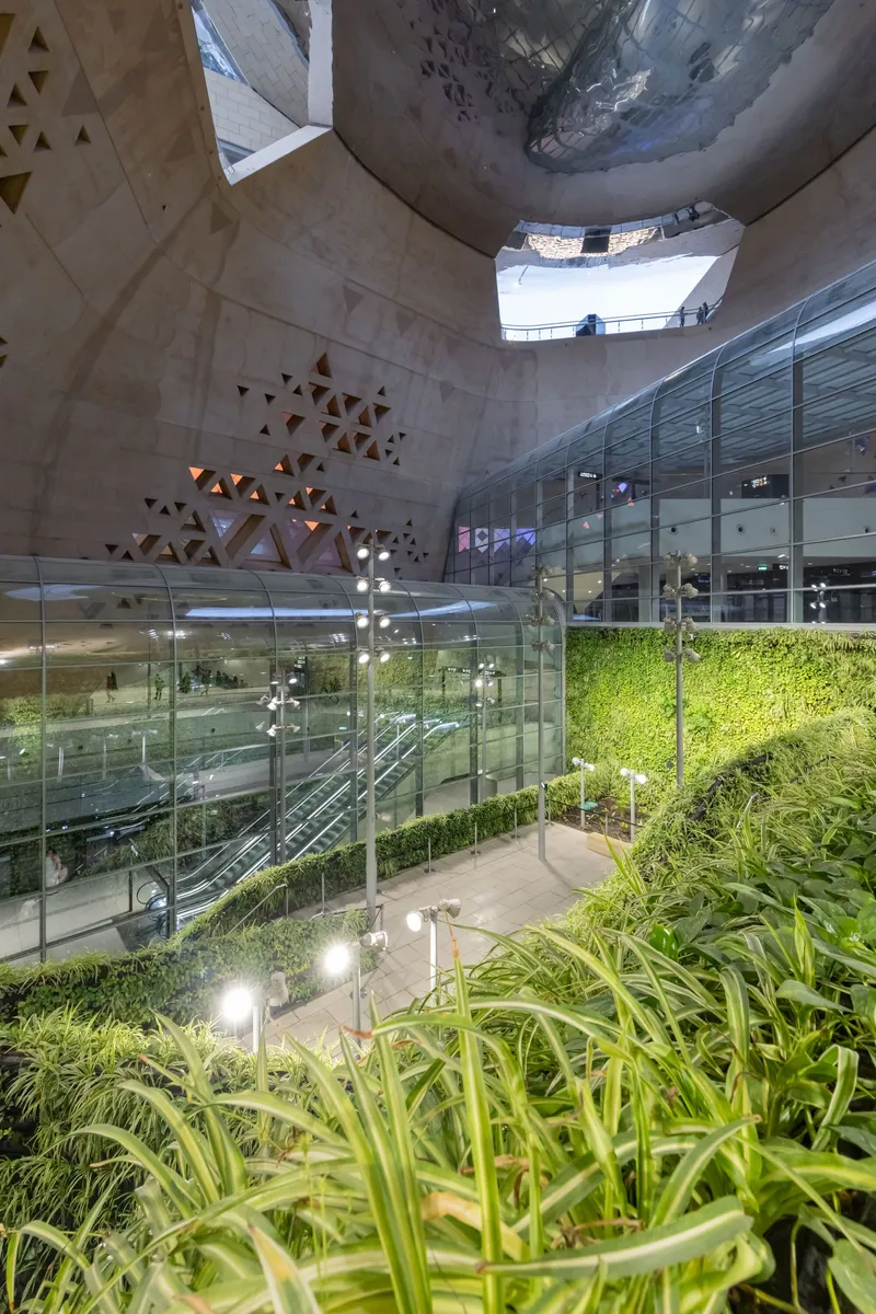 View up through the central atrium showing glass balconies, hanging lights, and planted terraces at dusk