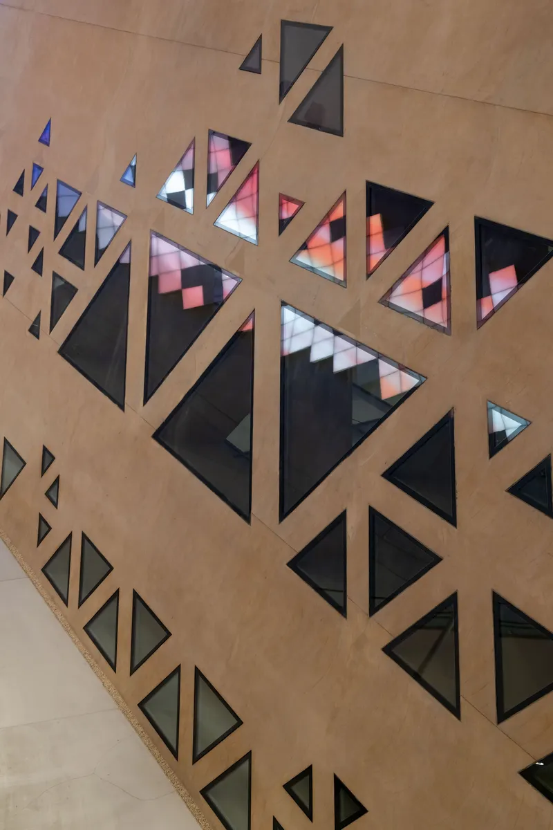 Close-up of triangular window openings in a concrete wall with colored glass reflecting interior light