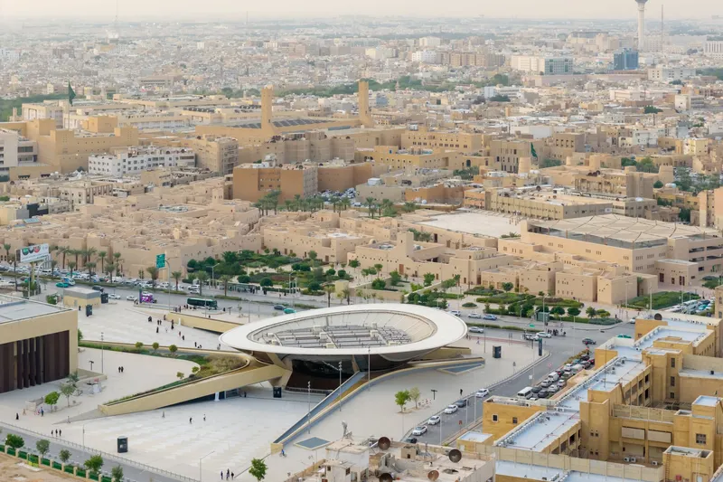 Elevated view of the circular rooftop oculus set within a vast paved plaza edged by palms and sand-colored buildings