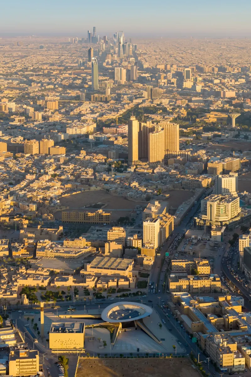 Aerial view at golden hour showing the circular rooftop opening surrounded by dense urban fabric and distant towers