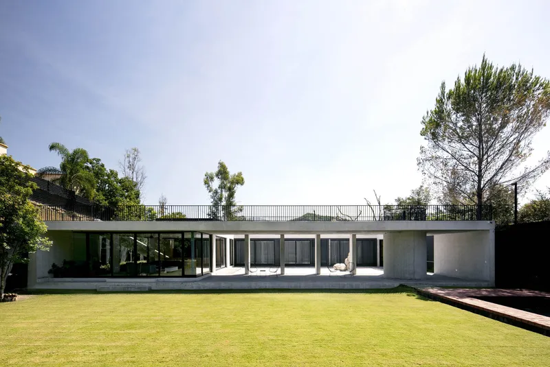 Garden facade with concrete columns and roof terrace railing framed by trees under clear skies