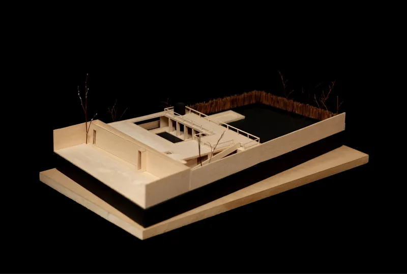 Physical model photographed against black showing courtyard house with screened enclosure and miniature trees