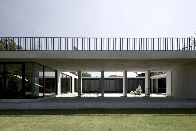 Concrete colonnade beneath a roof terrace with vertical metal railing and manicured lawn beyond