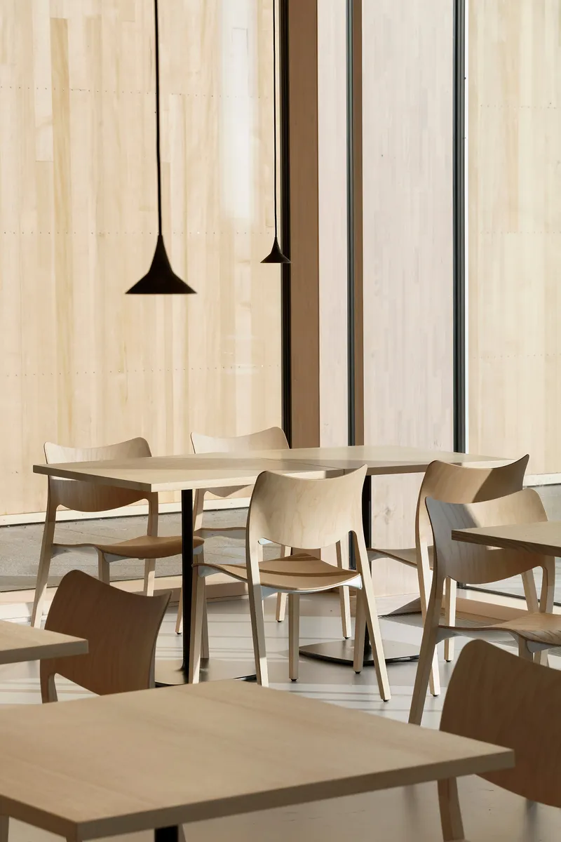 Dining tables with pendant lights hanging against a pale wood wall with dark vertical reveals