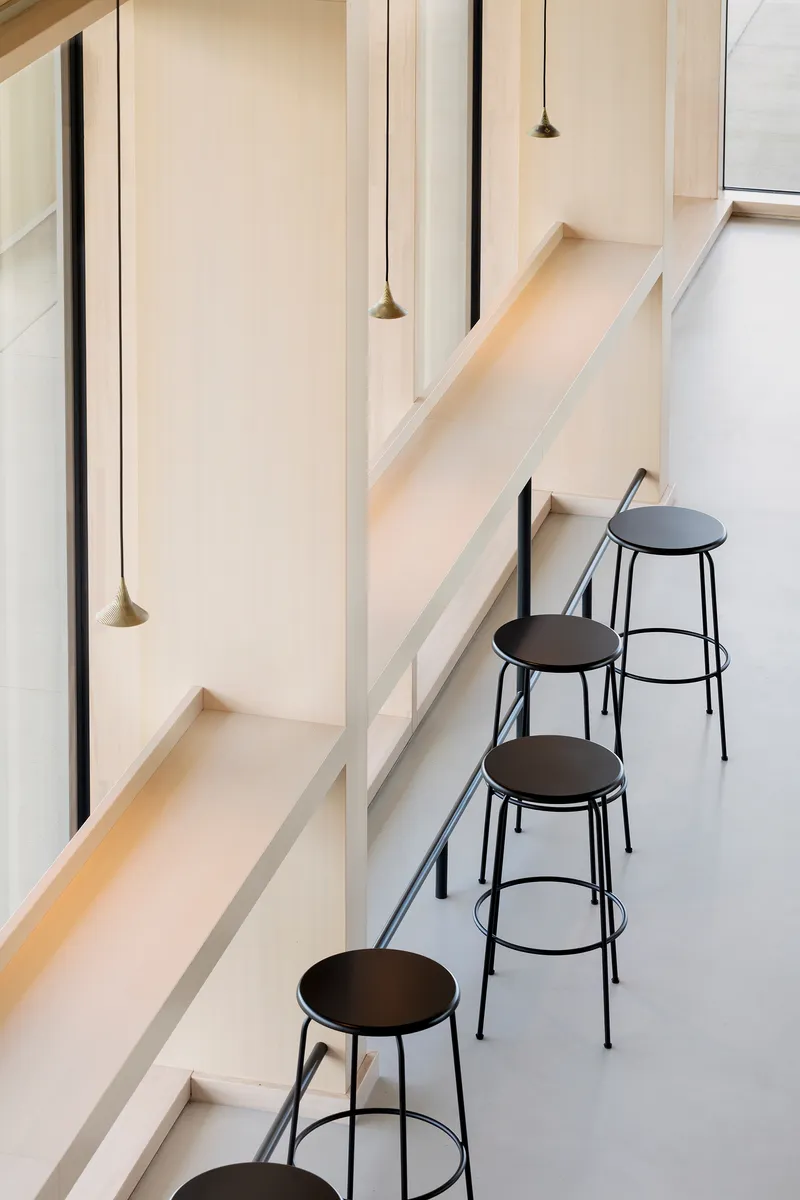 Four black metal stools beneath pale timber seating ledges and suspended conical pendant lights