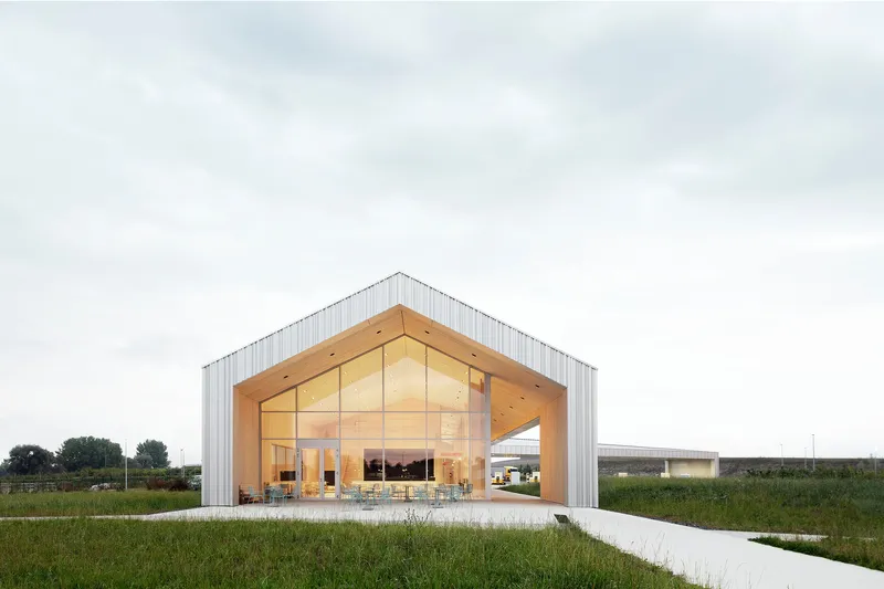 Glazed gable end revealing dining area with timber ceiling and tables under overcast sky