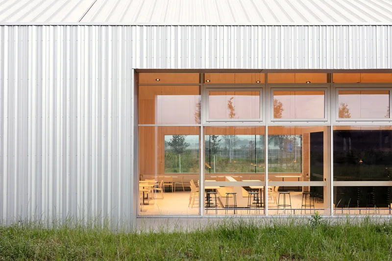 Floor-to-ceiling windows framed in timber showing interior dining tables beyond vertical metal cladding