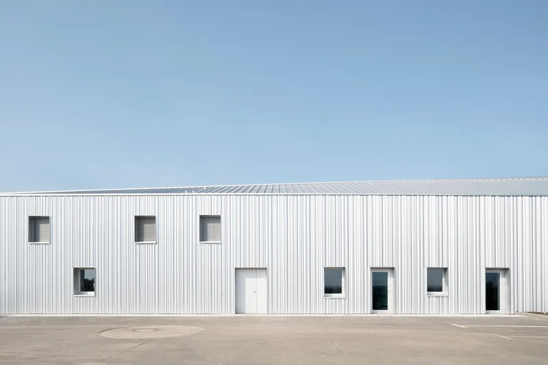 White ribbed facade with scattered rectangular window openings against a clear blue sky