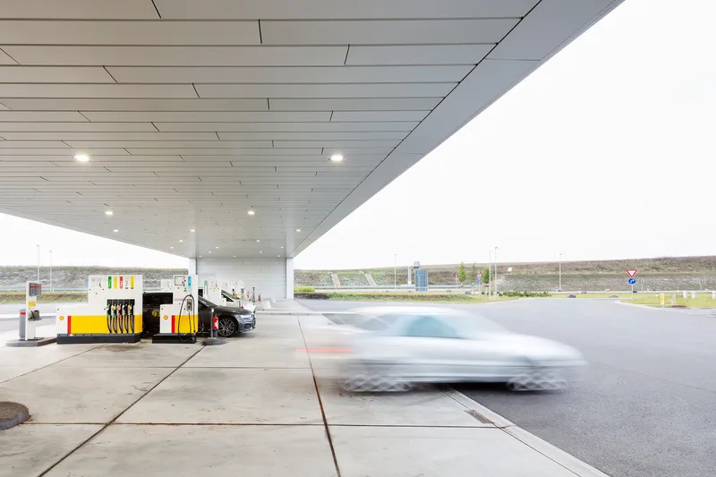 View beneath the canopy showing fuel pumps and a blurred car passing on the forecourt
