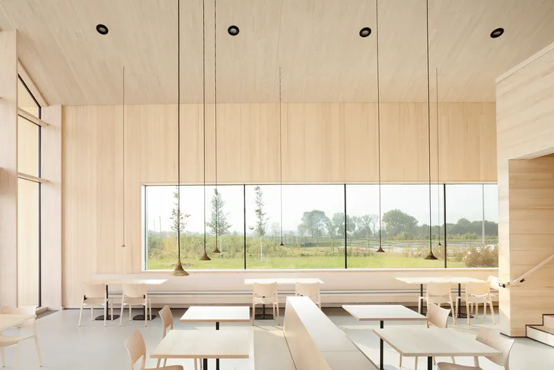 Timber-lined dining hall with hanging pendant lights and a horizontal window framing the landscape