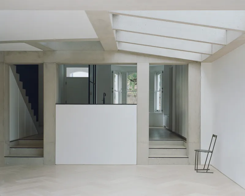 Interior room with concrete staircase and white kitchen volume beneath linear skylights