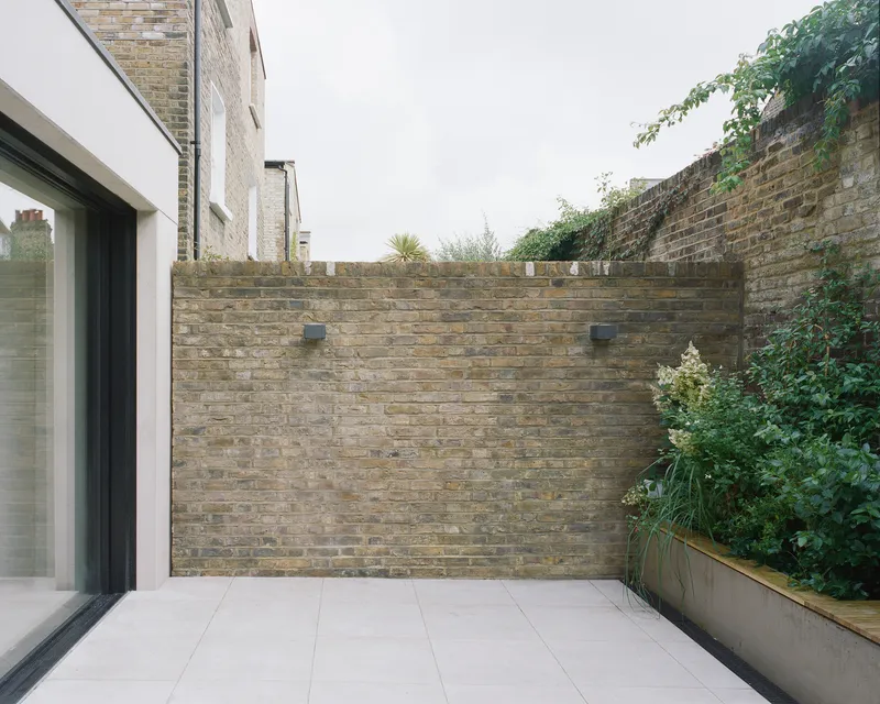 Rear courtyard terrace with buff brick walls and planted bed with greenery