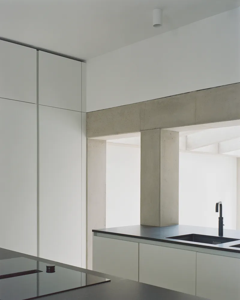 Kitchen corner showing concrete beam spanning across white cabinetry with dark countertop