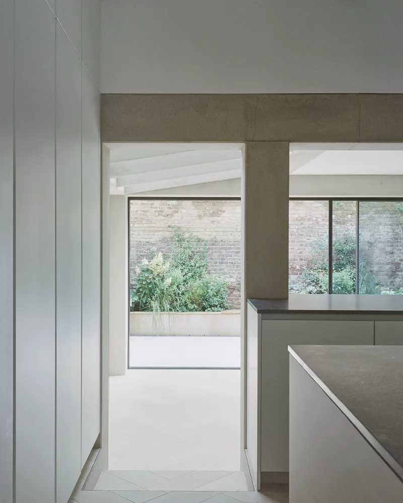 View through kitchen toward courtyard with planted greenery beyond glass doors