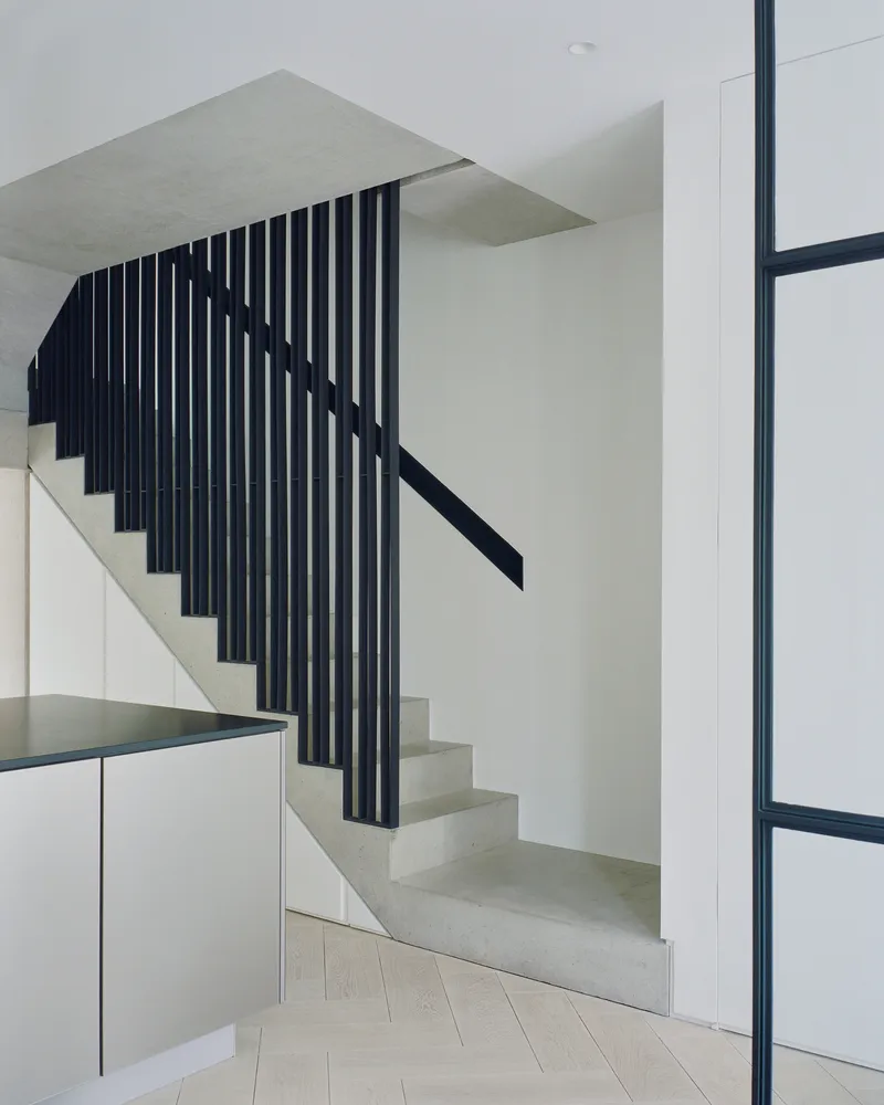 Concrete staircase with vertical black metal slat balustrade and metal handrail beside white cabinetry