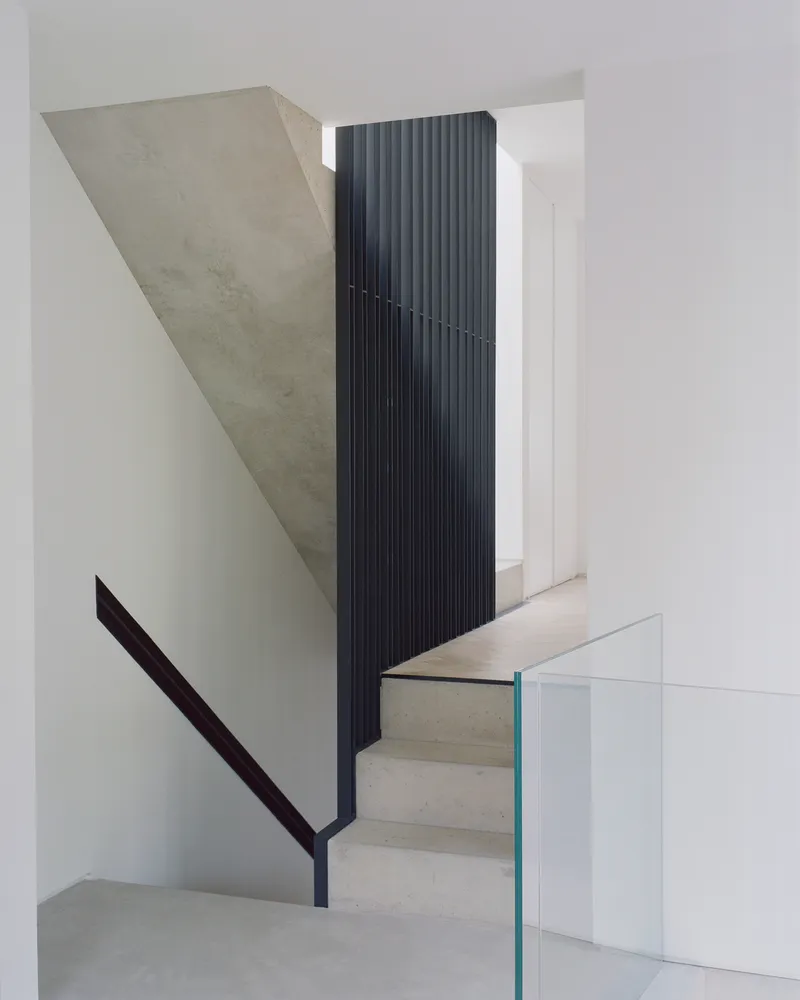 View of concrete stair landing with vertical black metal balustrade and glass guardrail below