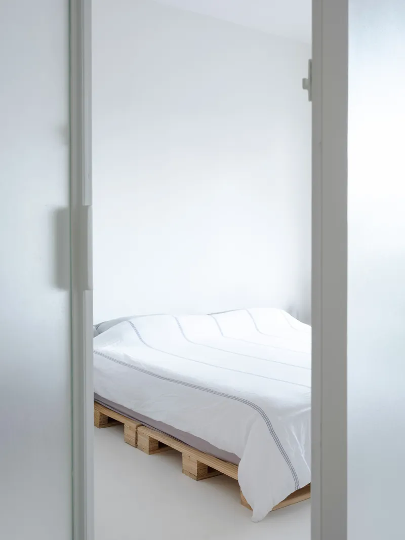 View through frosted glass doorway into bedroom with timber pallet bed and white bedding