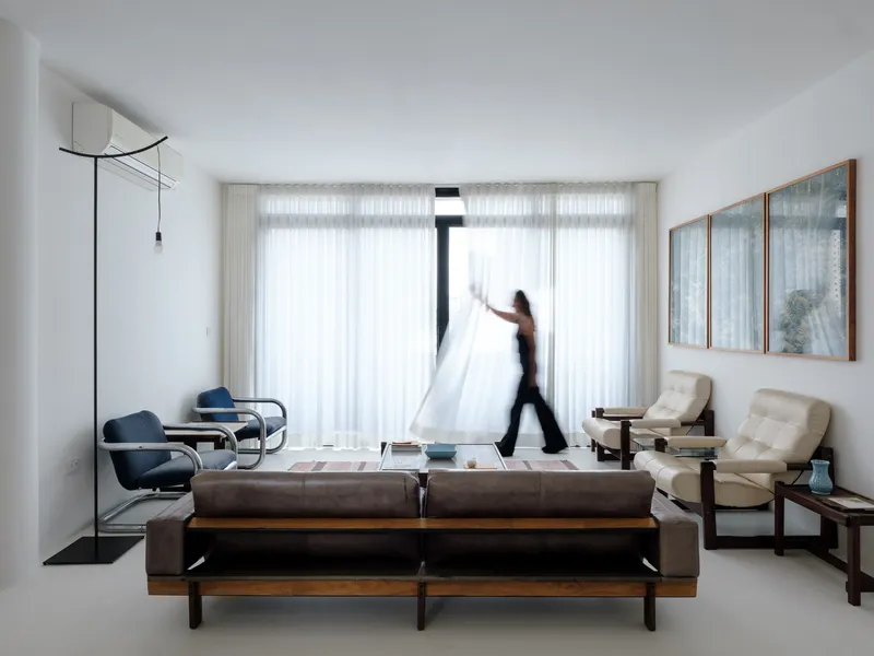 Living room with floor-to-ceiling sheer curtains and a person walking past the sofa