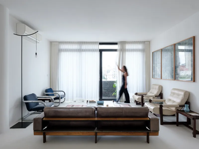 Living room with floor-to-ceiling sheer curtains and a figure crossing in front of the glazed balcony door