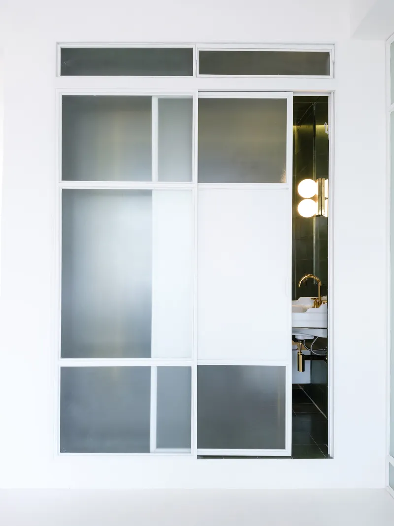 White-framed sliding door with frosted glass panels partially open to reveal a bathroom with brass fixtures
