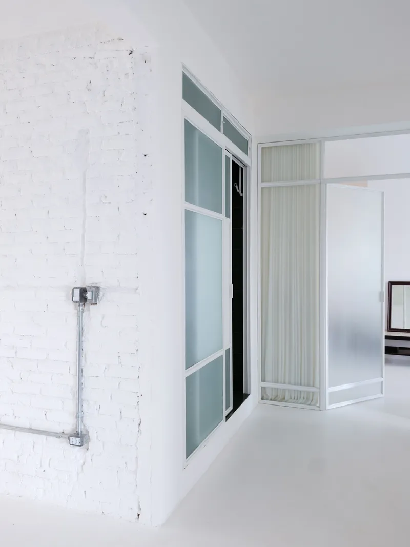 Interior partition with frosted glass panels and white frames against a painted brick wall with exposed conduit